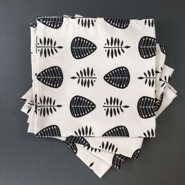 4 unbleached natural cotton napkins printed with a black leaf pattern. A grid pattern of four leaves in two designs, one more solid black with white veins and one of open black leaves. Four napkins set on a grey background