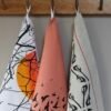 3 linen tea towels in various patterns hanging from a a row of hooks