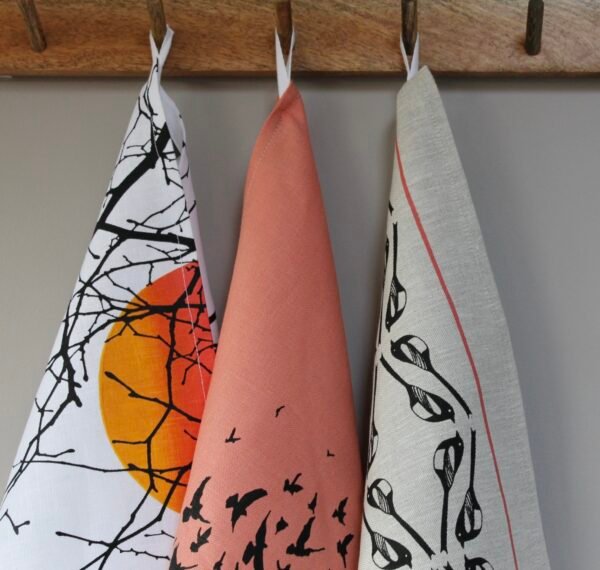 3 linen tea towels in various patterns hanging from a a row of hooks